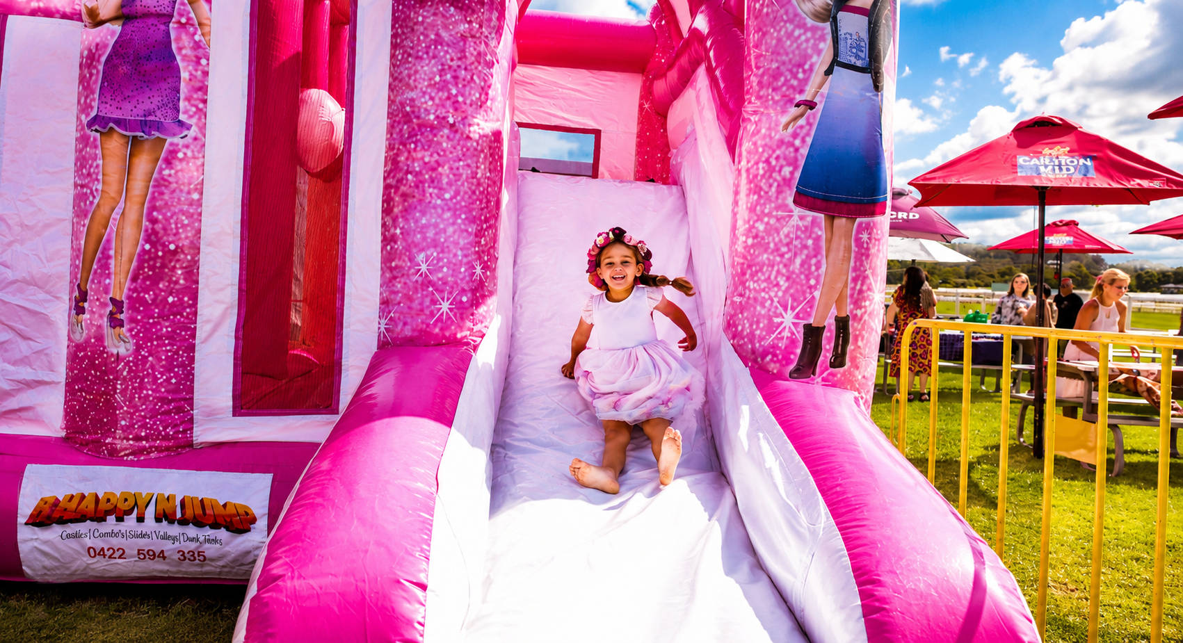 Little girl sliding down a pink Barbie bouncy castle slide