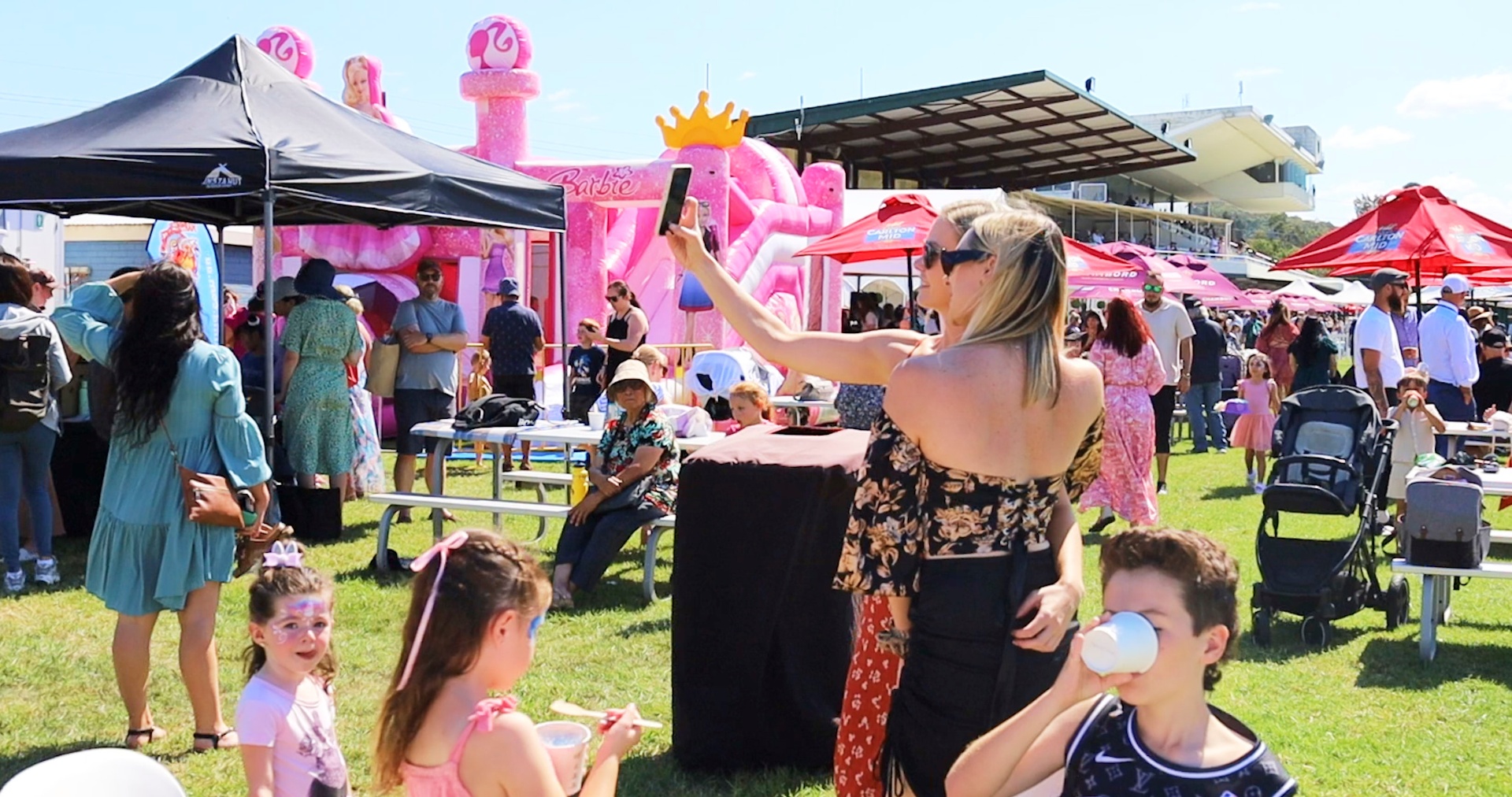 Families enjoying a sunny Easterfest with pink Barbie inflatable castle and food stalls